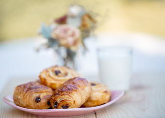 French croissant and buns with raisins, a glass of milk on wooden table.  Bouquet of flowers. Dessert. Image doesn’t in focus. Soft focus. Nature wallpaper blurry background. Copy space.