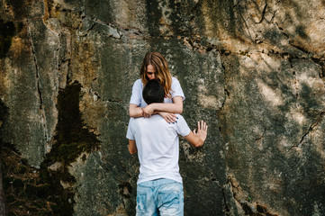 A man and woman stand and hug, kiss near large rock. stone. A young, stylish, love couple looks back  at each other, upper length. Close up. Nature autumn. Side view.