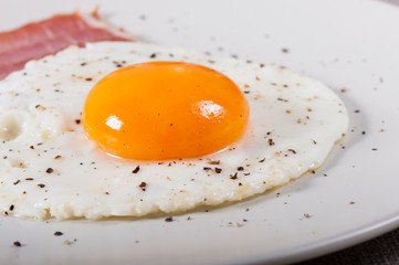 Fried egg and bacon on a light plate, breakfast food.