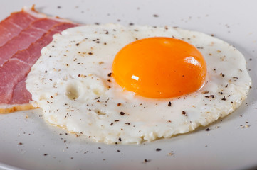 Fried egg and bacon on a light plate, breakfast food.