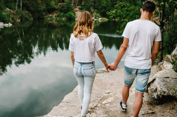 Legs young couple going on stone near lake. full length. Man's and woman's view from the back on...