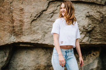 Slim girl stands and poses at cliff. Portrait of a woman in jeans and a white T-shirt, against the background of the mountain on nature. upper half. Looking sideways. Close up