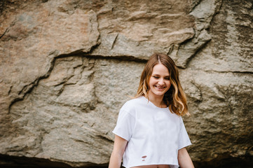 Slim girl stands and poses at cliff. Portrait of a woman in white T-shirt, against the background of the mountain on nature. upper half. Looking down. Close up
