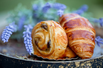 Bun with raisins and french croissant on old wine barrel. Dessert. Lavender flowers. Dinner in a garden in summertime. Summer twilight. Soft focus. Blurry background. Close-up. Macro.