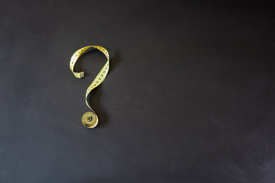 Tape measure forming the shape of question mark on chalkboard