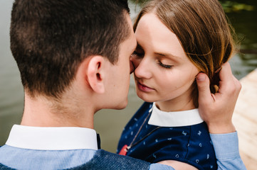 The face of young people. A couple standing, hugging, kissing on the background lake and on a wooden bridge. Close up. headshot, half length. A woman with Make-up her eyes closed.