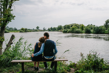 A young couple sitting back on the bench, kissing and hugging  near lake. Nature, landscape. View back. Close up.