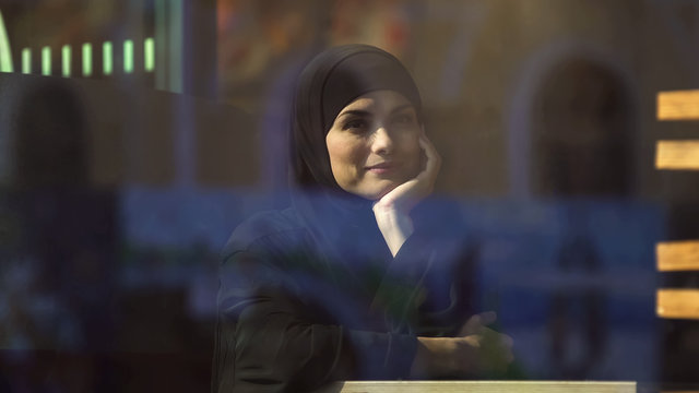 Beautiful thoughtful Muslim lady sitting in cafe wearing hijab waiting for order