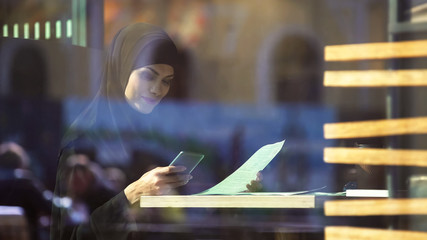 Fototapeta na wymiar Beautiful Muslim lady freelancer working in cafe, chatting with partner on phone