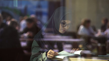 Young Arabic lady reading book in cafe, student preparing for exams, literature