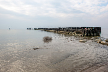 calm sea beach in summer with large rocks and wooden poles from old breakewater in the sea