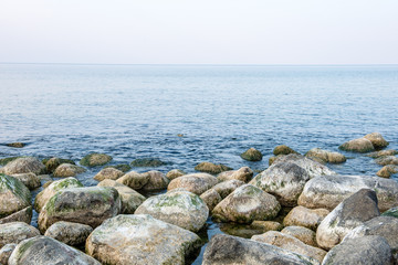 calm sea beach in summer with large rocks and wooden poles from old breakewater in the sea