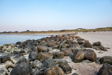calm sea beach in summer with large rocks and wooden poles from old breakewater in the sea
