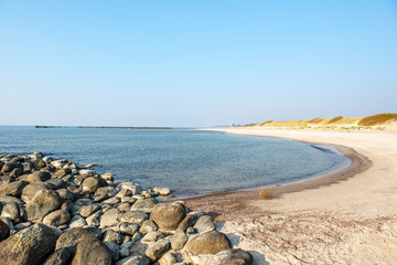 calm sea beach in summer with large rocks and wooden poles from old breakewater in the sea