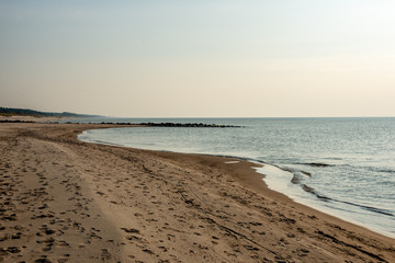 calm sea beach in summer with large rocks and wooden poles from old breakewater in the sea