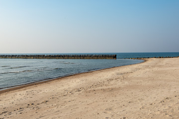 calm sea beach in summer with large rocks and wooden poles from old breakewater in the sea