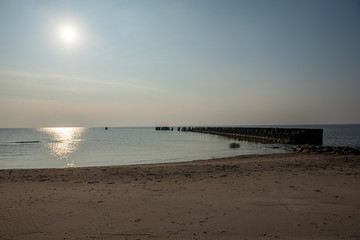 calm sea beach in summer with large rocks and wooden poles from old breakewater in the sea
