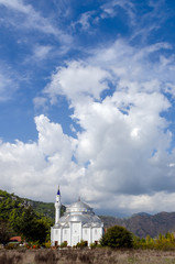 Huge white mosque with one minaret against the blue cloudy sky and mountains at Cirali, Turkey