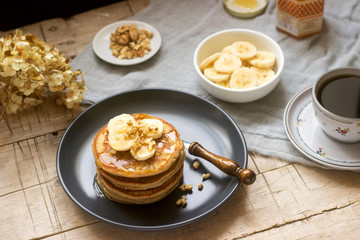 Pancakes with banana, nuts and honey, served with tea. Rustic style.