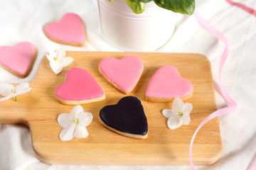 Pretty  girlish flat lay with gently pink hearts cookies and 1 black heart cookie with white violets blooming flowers and satin ribbon.14 february valentine's day and wedding bonboniers gift treat