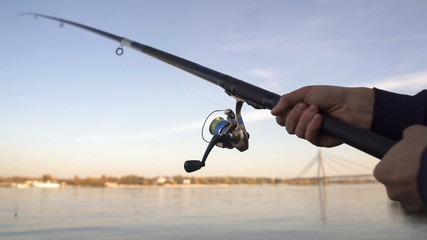 Obraz premium Spinning rod closeup, man fly-fishing near river, active leisure, weekend