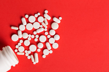 Assorted pharmaceutical medicine pills, tablets and capsules. Red background.