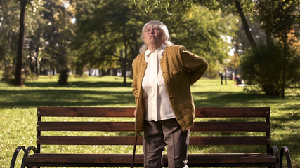 Fototapeta premium Mature woman feeling back pain standing up from park bench, health problems