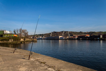 the river of Barakaldo where we see two fishing poles, and in front of the river are the cranes and sestao factories