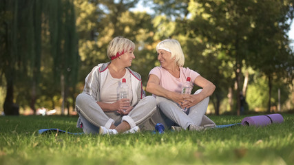 Women chatting sitting on grass after yoga classes on fresh air, healthcare