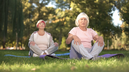 Senior women doing breezing exercises sitting in lotus position in park, energy
