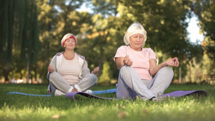 Elder women sitting in lotus position and meditating doing yoga in park, energy