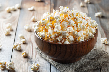 A wooden bowl of salted popcorn at the old wooden table. Dark background. selective focus - Powered by Adobe