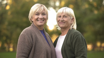 Cheerful mature females hugging smiling into camera, enjoying pastime outdoor