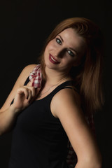 Low key portrait of happy young attractive woman on the black background. Woman is holding a checkered shirt over her right shoulder. Vertically. 