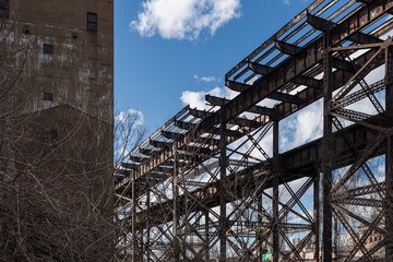 Rotting elevated steel train tracks passing an abandoned factory in a depressed urban industrial area