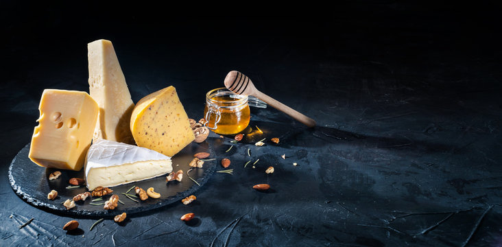 Different kinds of cheese with nuts and honey on dark background, copy space