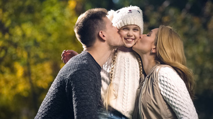 Fototapeta premium Happy parents kiss cheerful daughter in autumn park, wealthy family, wellbeing