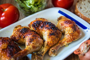 Roasted chicken legs with salad and bread on wooden table
