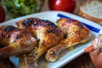 Roasted chicken legs with salad and bread on wooden table
