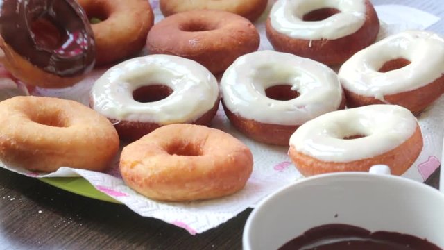 A woman dips American donuts, fried in sunflower oil, into melted chocolate...
