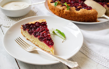 Homemade cherry pie served with cream on a light background with cherry leaves and flowers.