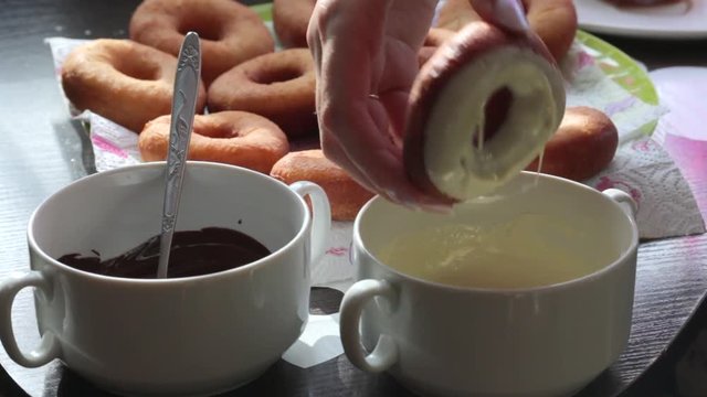 A woman dips American donuts, fried in sunflower oil, into melted chocolate.