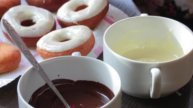 A woman dips American donuts, fried in sunflower oil, into melted chocolate..
