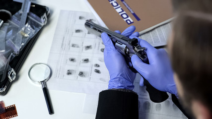 Police officer checking revolver sitting table, crime scene evidence, ballistics