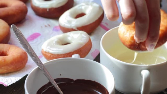 A woman dips American donuts, fried in sunflower oil, into melted chocolate