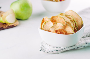 Dried apple slices in a white ceramic bowl on light background