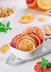 Mixed dried citrus orange and grapefruit slices in a white ceramic bowl on light background. Selective focus.