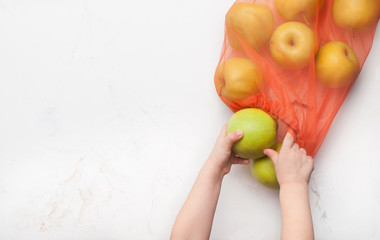 Kids hands taking an apple from eco-friendly shopping bag