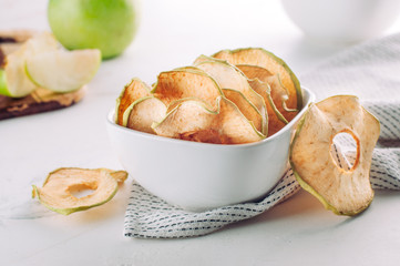Dried apple slices in a white ceramic bowl on light background