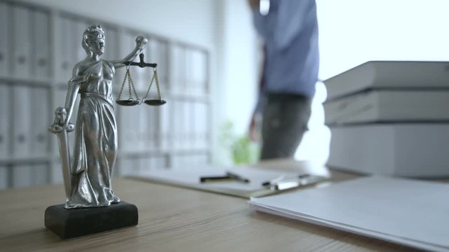 Lawyer talking on mobile phone in law office, selective focus on statue of Lady Justice